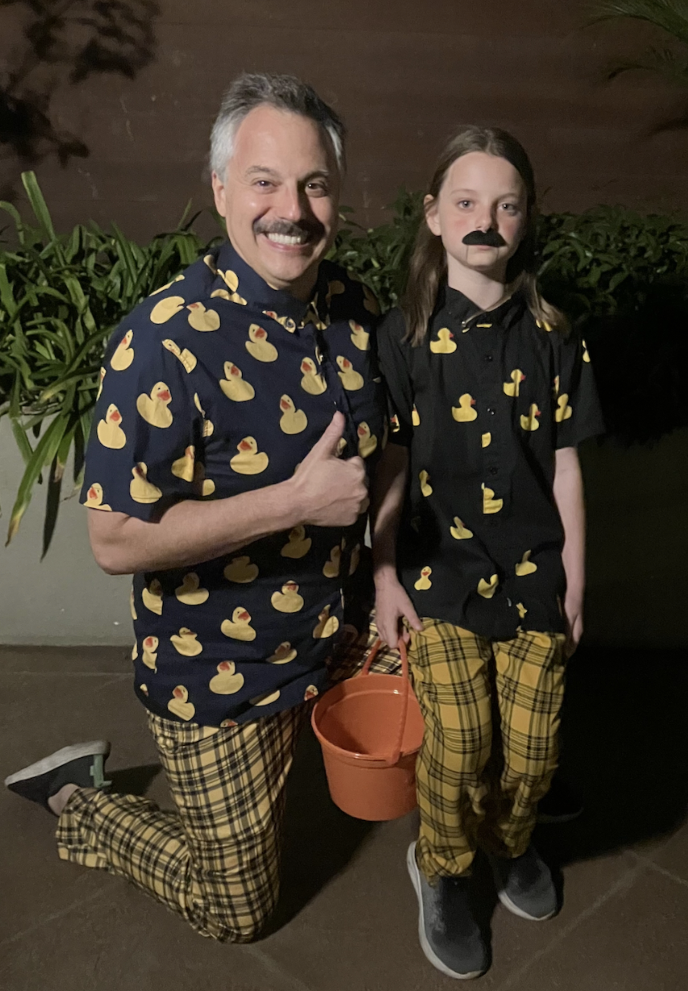May contain two people in matching Dennis duck shirts and plaid pants, one holding an orange bucket.